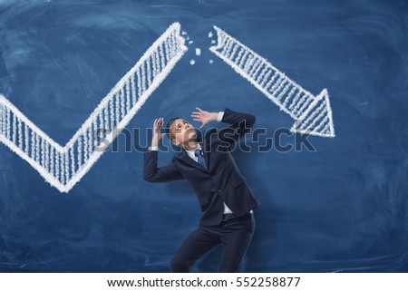 Businessman cowering on blue blackboard background with chalk drawing of white statistic arrow broken in half. Business management. Profit and loss. Business and success. Royalty-Free Stock Photo #552258877
