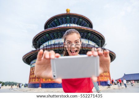 Tourist taking goofy face funny selfie on travel. Happy young woman having fun with mobile phone at famous Beijing landmark. Temple of Heaven China travel.