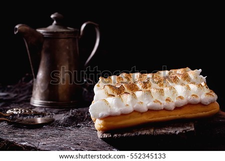 Home made eclairs decorated with white meringue on the rustic wooden serving board with a metal coffee pot black background. Dark Rustic style.