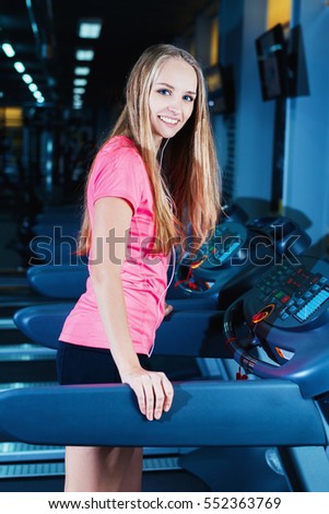 Attractive fitness girl running on machine treadmill. Pretty girl doing workout at modern fitness gym