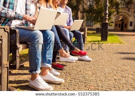 close-up photo of  diverse students sitting on bench and study up with device