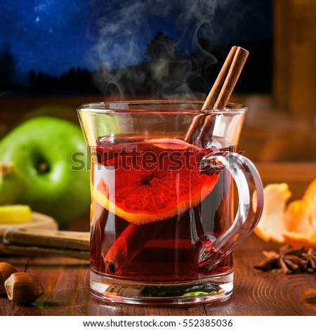 Traditional winter holiday alcoholic drink. Mulled wine with lemon slice on a table. Starry night winter landscape in a window.