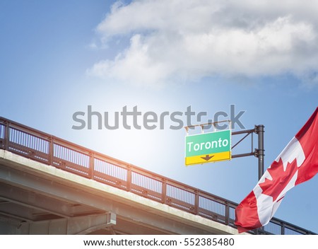 Destination Toronto, Ontario, Canada sign on highway with Canadian flag waving beside