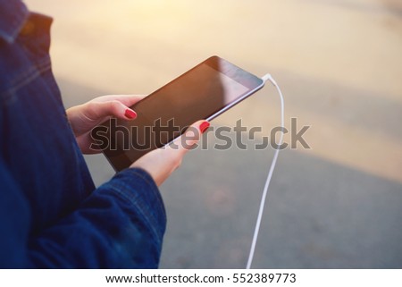 Cropped image of female hands holding modern portable pc while listening to favorite music via tablet with mock up screen standing outdoors near copy space area for your advertising messages,content