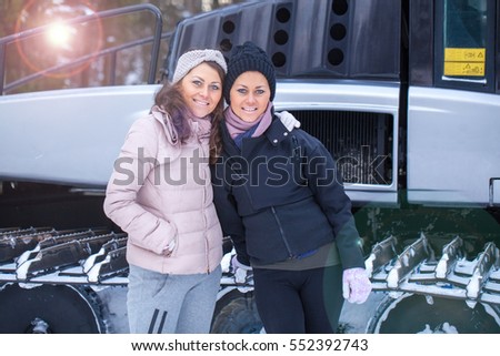 Twins posing on ski resort with snow groomer mashine on background
