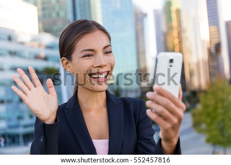 Businesswoman taking selfie photo using smart phone app on smartphone for social media wearing suit jacket outdoors.  