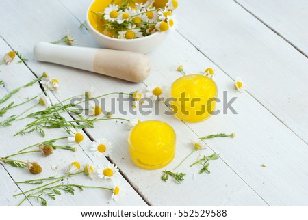 medical cream and daisy herbal flowers on white wood table background