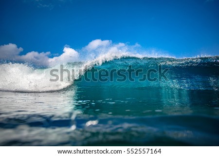 Front view of Big ocean wave in daylight. Blue sky with clouds. 
Sea swell for surfing sport activity. Nobody on picture. Vibrant bright tropical colorful image with copy space on a water surface.