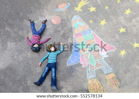 Two Funny little kid boys flying in universe by a space shuttle picture painting with colorful chalks. Creative leisure for children outdoors in summer. Friends having fun together