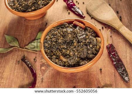 A photo of a lentil stew, shot on a dark wooden texture with bay leaves and peppers scattered around