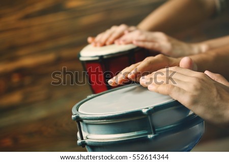 Hands of man playing African drum on brown blurred background Royalty-Free Stock Photo #552614344
