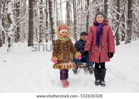Two granddaughter ride with grandpa in the winter woods on a sled. Beautiful Christmas vacation with active grandparents.