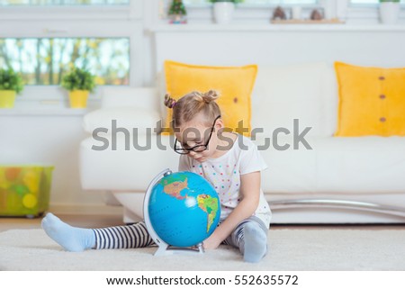 Pretty child girl at home dreaming of travel and tourism, exploring the world map and globe