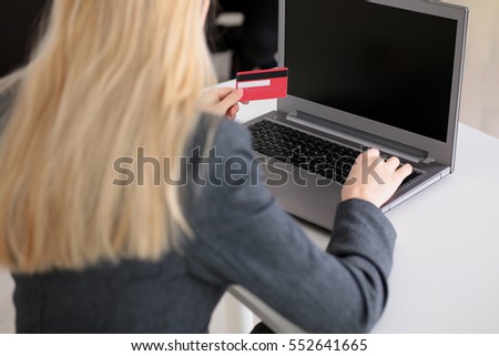Woman holding credit card in hand and entering security code using laptop keyboard, photo with depth of field