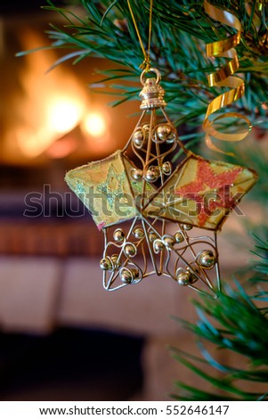 A large goden star toy. Christmas toys on the Christmas tree near the burning fireplace. Christmas toys in the form of golden shiny star.