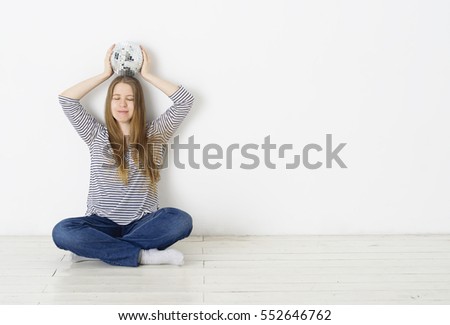 Young pretty girl sitting near white wall with disco ball in her hands.Meditating with closed eyes and preparing to party.