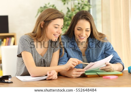 Two students doing homework together and helping each other sitting in a table at home with a homey background Royalty-Free Stock Photo #552648484