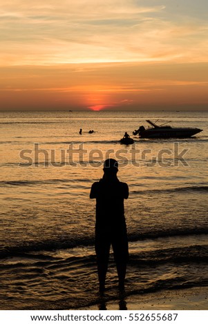 Man taking picture people swim near shadow boat and light sunset on the beach