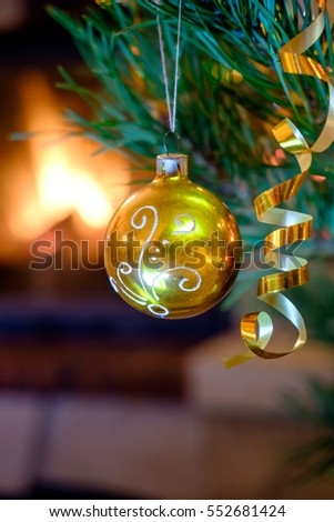 Big yellow glass ball with heart pattern. Christmas toys on the Christmas tree near the burning fireplace. Christmas toy in the form of red bowl with heart. 