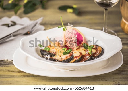 Salad of baked eggplant with cheese and a glass of wine close-up on a wooden table.