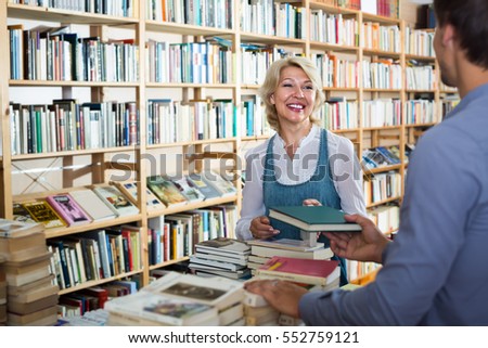 portrait of glad mature woman talking to assistant in book store
