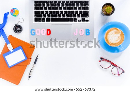 Caption word  Good Job on laptop. White office desk with laptop, diary, eyeglasses, compass, pen, blank identification card and cup of coffee.Top
