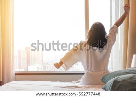 Easy lifestyle Asian woman waking up from good sleep in weekend morning taking some rest, relaxing in comfort bedroom at hotel window, having happy lazy day enjoying work-life quality balance concept Royalty-Free Stock Photo #552777448