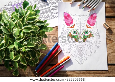 Composition of colouring pictures and pencils on wooden table