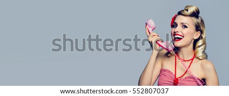 Portrait of beautiful young happy smiling woman with phone, dressed in pin-up style. Caucasian blond model posing in retro fashion and vintage concept studio shoot. Horizontal banner composition.
