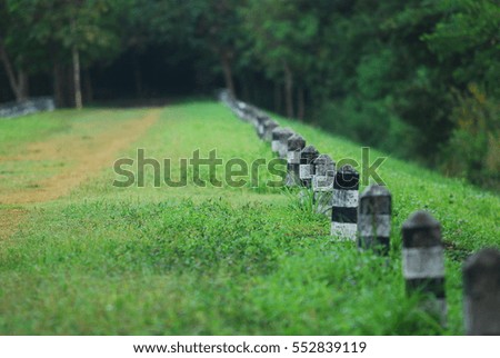 Row of black and white short pillar in the fresh green grass field for direction to forest