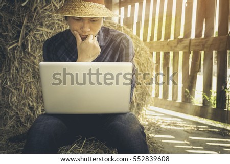 Young farmer in barn with laptop computer against hay background.