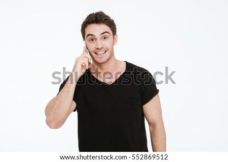 Picture of cheerful young man dressed in black t-shirt standing over white background talking by his phone.