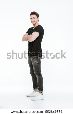Picture of attractive cheerful young man dressed in black t-shirt standing with arms crossed over white background.