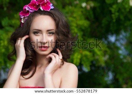Outdoor summer portrait of very beautiful young woman in vacation with pink orchids in the hair and green natural background