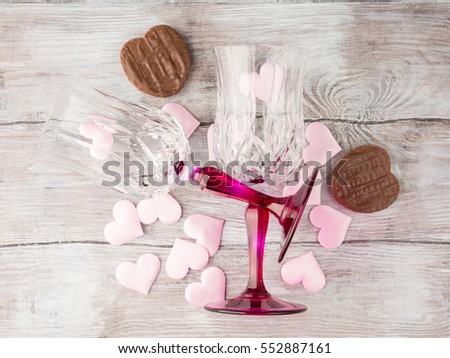 Two stemmed champagne glasses with pink hearts and chocolate cookies on wooden textured background. Valentine's day wedding romantic date invitation. Top view
