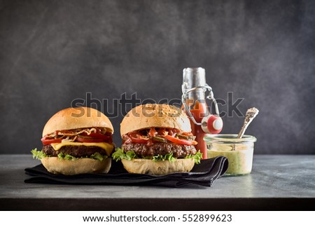 Green dipping sauce beside a cheese burger and beef patty on a sesame seed bun