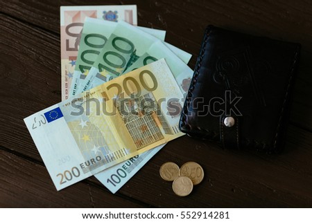 Wallet and Euro cash. Brown male wallet and euro banknotes with euro cents on wooden background.