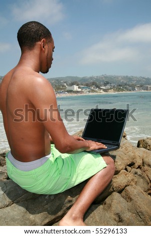 a young man uses his laptop computer while at the beach outdoors