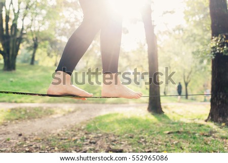 Close up on feet walking on tightrope or slackline outdoor in a city park in back light - slacklining, balance, training concept  Royalty-Free Stock Photo #552965086