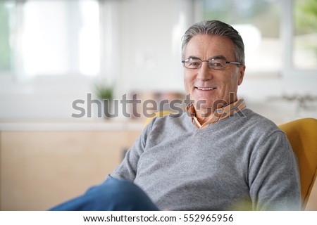 Smiling senior man with eyeglasses relaxing in armchair Royalty-Free Stock Photo #552965956