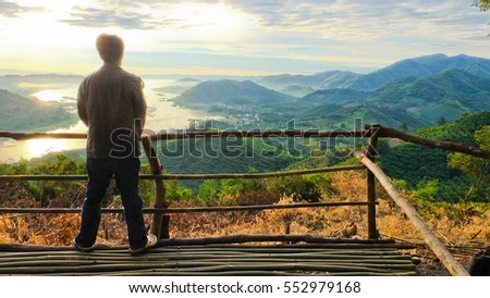 A man standing to see sunrise landscape with sea of fog above Mekong river at Phu Huai Isan mountain viewpoint in Nong Khai Province, Thailand Royalty-Free Stock Photo #552979168