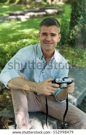 Happy smiling photographer at the park, he is sitting and holding a digital camera