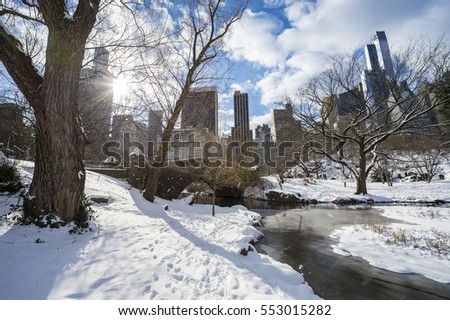 Cold wintry view of the old stone Gapstow Bridge in Central Park, New York City, with the skyscrapers of Midtown Manhattan casting long shadows in the background