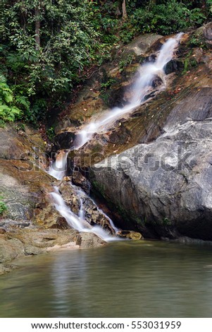 A beautiful scenery of tropical waterfall flowing through the beautiful tropical green forest with rock cover with moss. Image contain excessively noise/sharp or blur due to long exposure. 