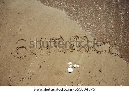 Word Summer written on a sandy beach.