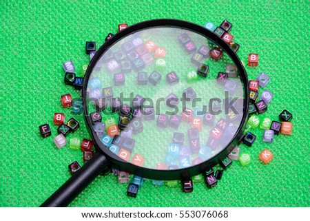 Multicolored wording cubes and magnifying glass on green background.