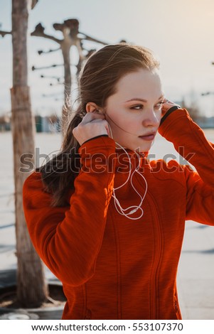 Young female sportswoman listening music in earphones