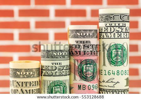 rising steps made of rolls of four most valued american dollar banknotes in one row on red brick background