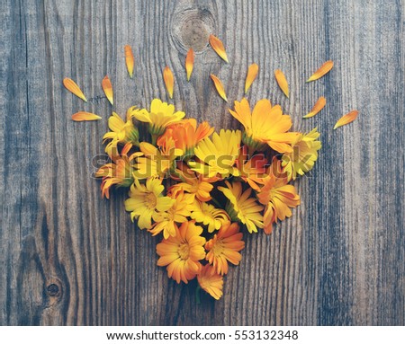 Yellow summer flowers in the form of heart on a wooden board in vintage tones. Calendula flowers. Festive romantic background