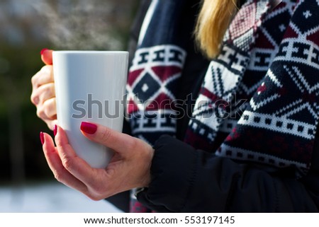 woman holding a steaming hot cup of coffee in her hands outdoors in winter, numbed female hands with polished nails